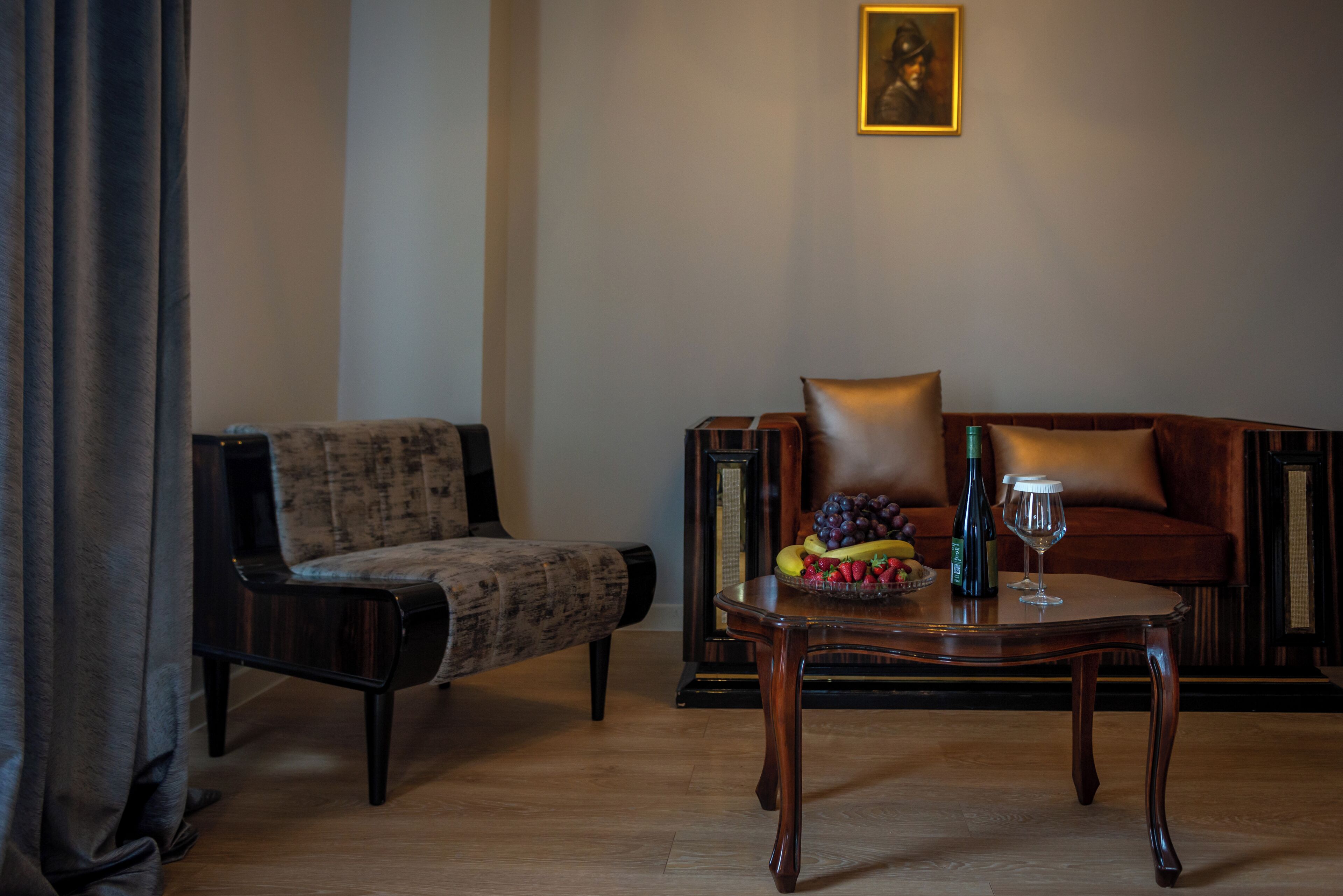 A room with a sofa, a chair, a table with fruit and a bottle, and a framed picture on the wall.