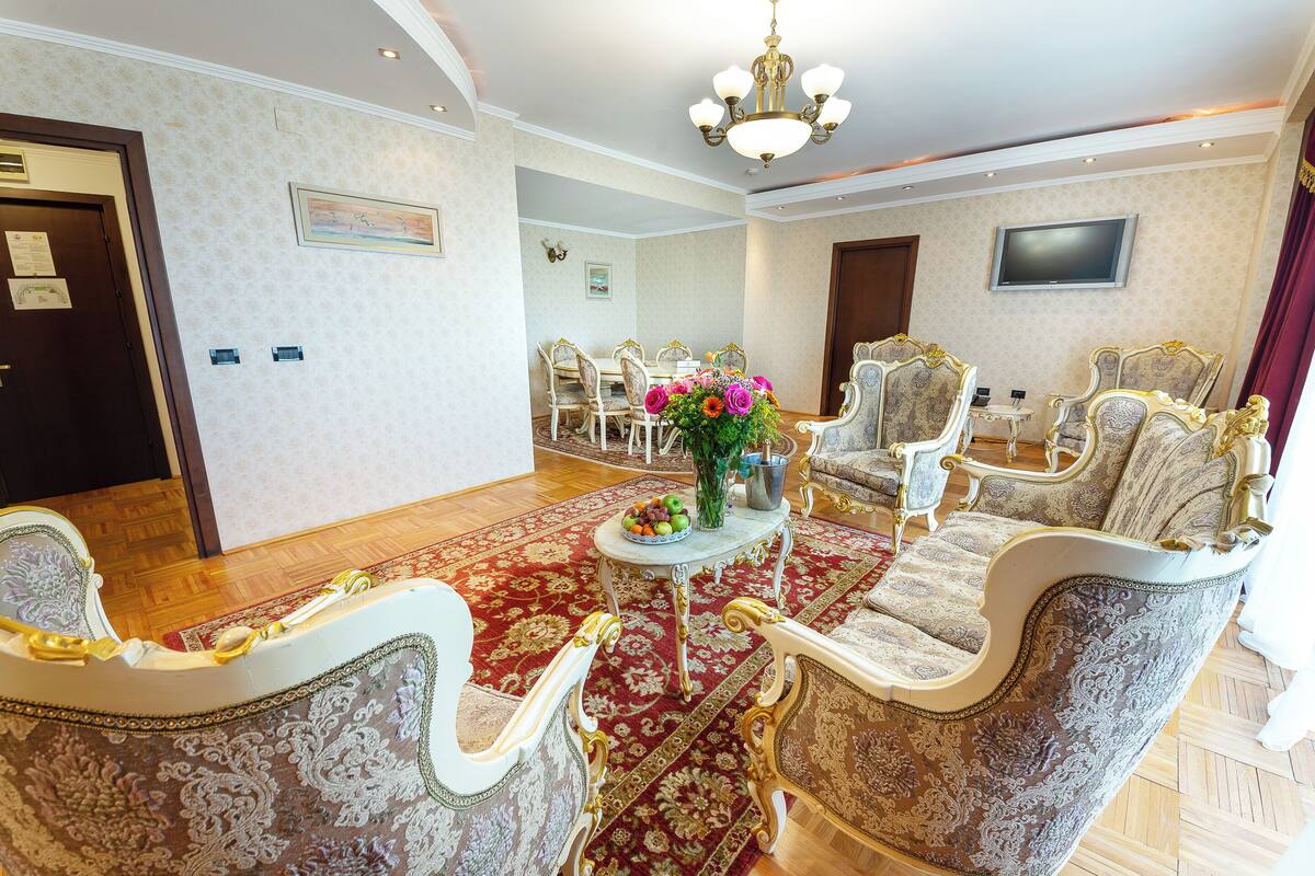 Quarto com mobiliário requintado, um lustre, uma televisão e um tapete vermelho.