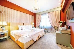 A hotel room with a large bed, bedside tables, a desk, a chair, a TV, and a chandelier. - Phoenicia Grand Hotel (Bucharest)