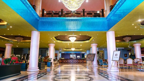 Un vestíbulo de hotel con mostrador de recepción, columnas imponentes, una araña de cristal y un suelo con diseño.