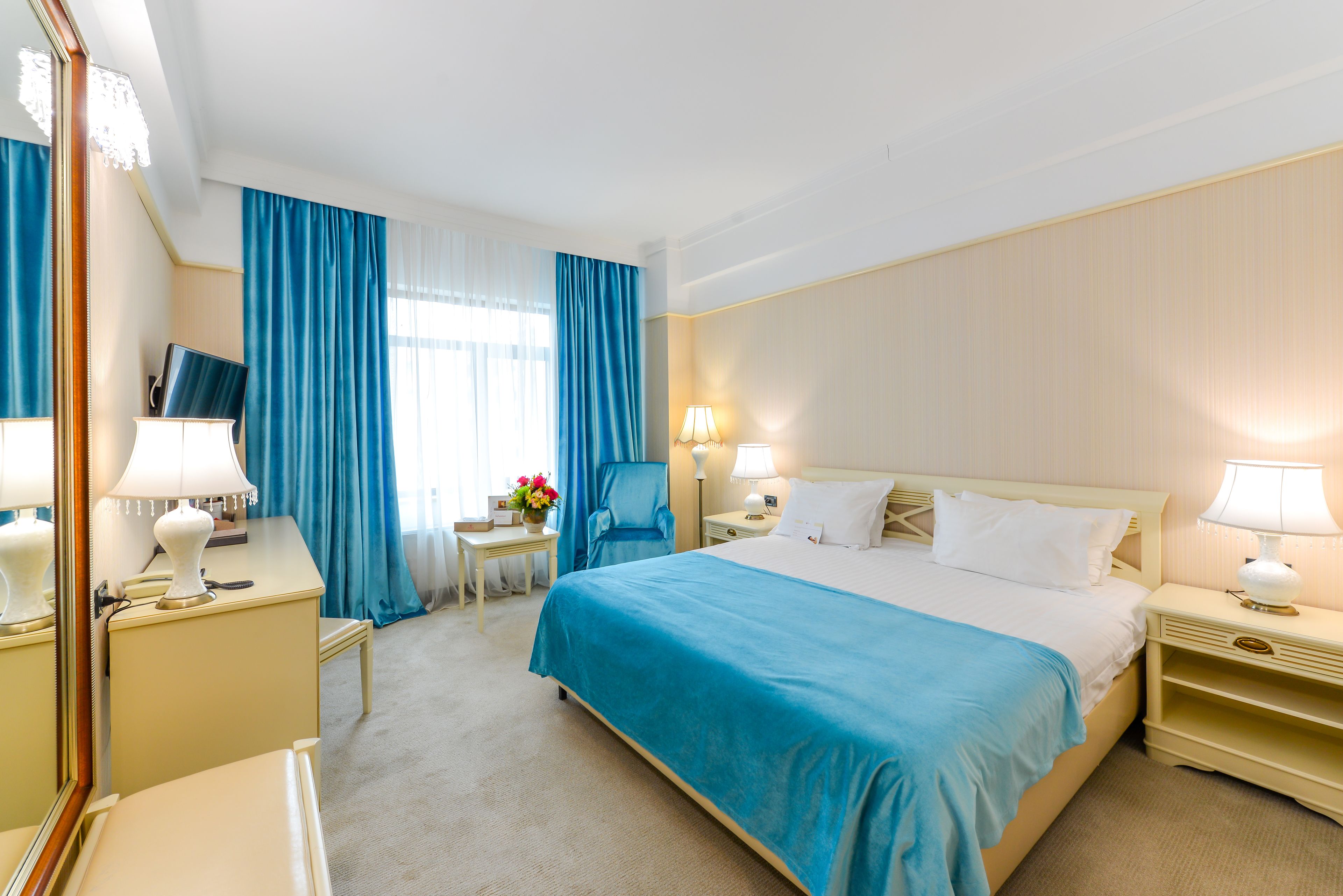 Habitación de hotel con una cama grande, un escritorio con lámpara, una silla y un televisor.