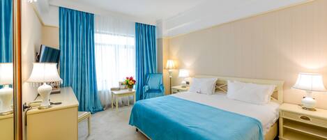 Habitación de hotel con una cama grande, un escritorio con lámpara, una silla y un televisor.