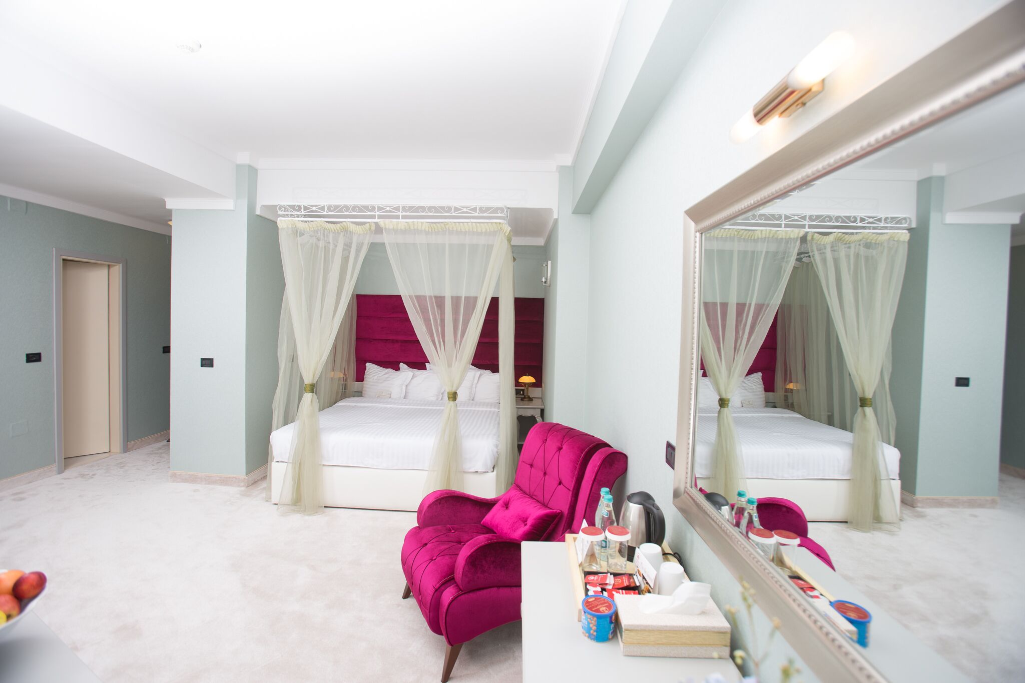 A hotel room with two beds, a large mirror, a vanity with toiletries, and a pink armchair.