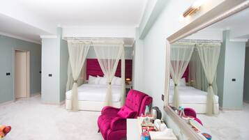 A hotel room with two beds, a large mirror, a vanity with toiletries, and a pink armchair.