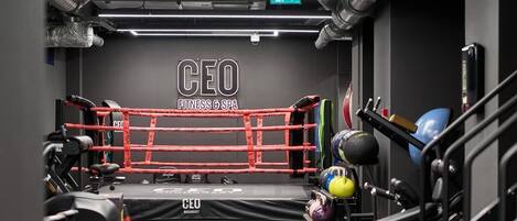 Une salle de sport équipée d’un ring de boxe, de matériel d’exercice et d’une enseigne indiquant « CEO FITNESS & SPA ».