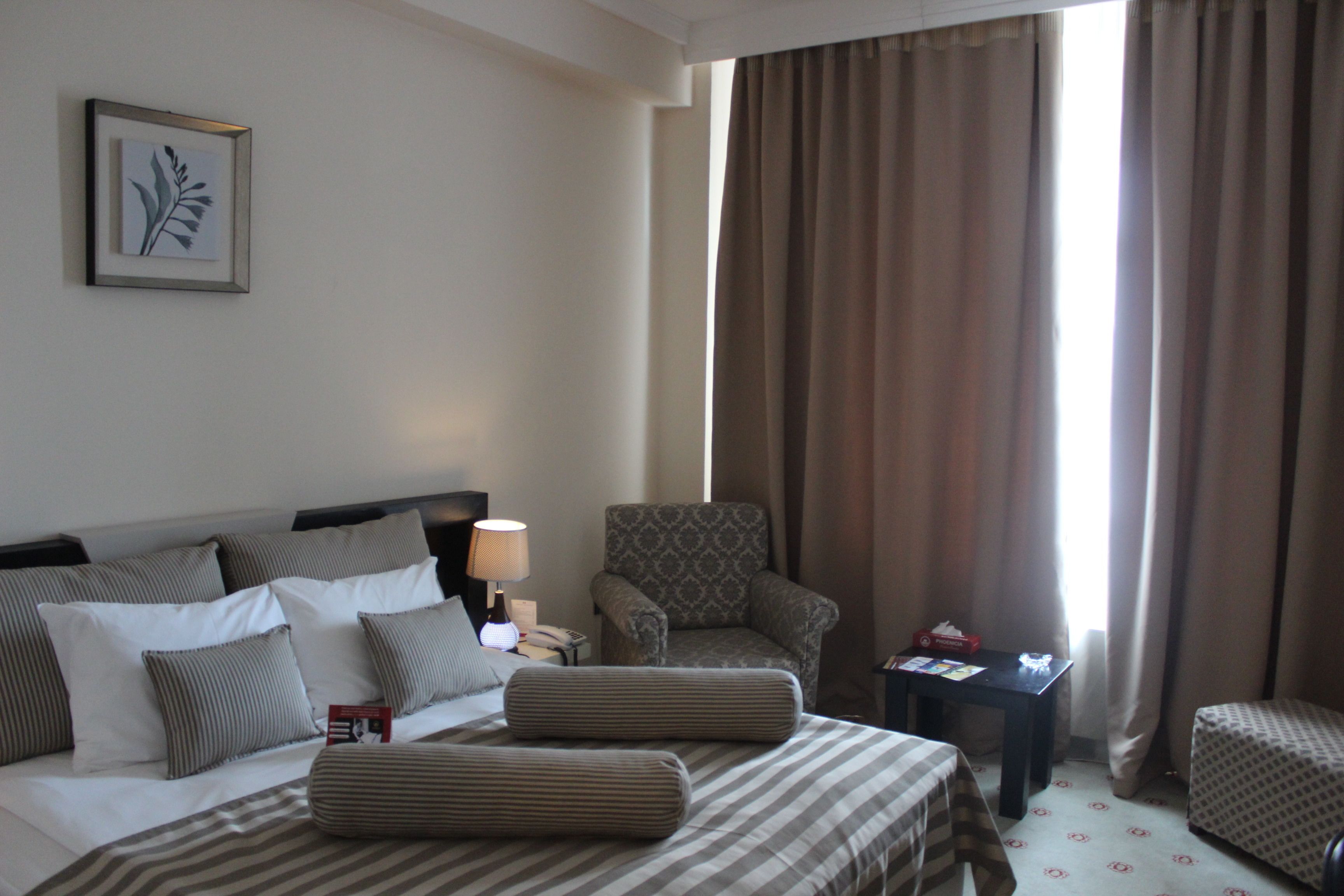A hotel room with a bed, a chair, a small table, and a window with curtains.