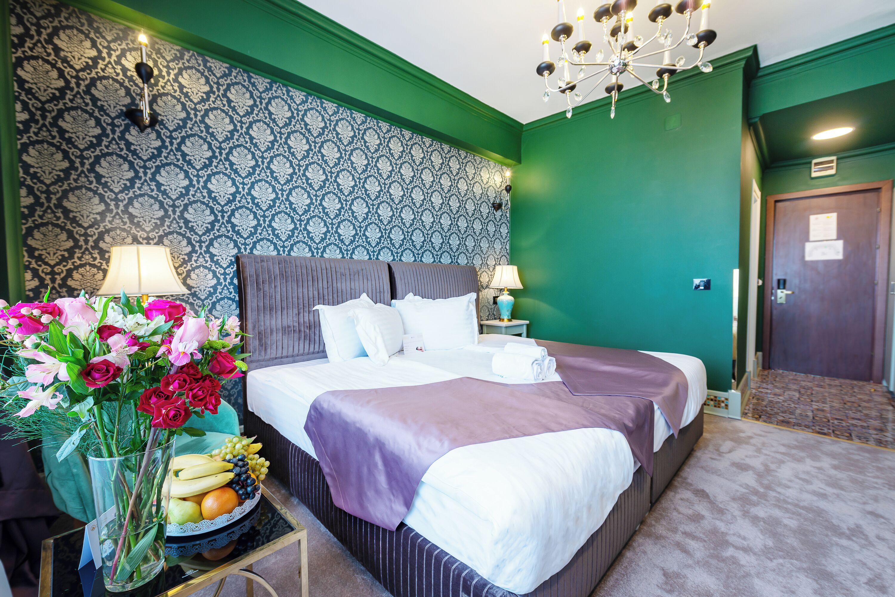 Une chambre d’hôtel avec un grand lit, deux tables de chevet avec des lampes, un vase de fleurs et un panier de fruits.