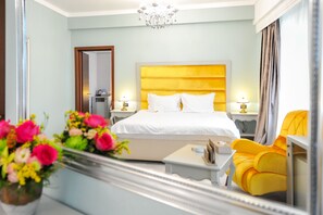 A hotel room with a large bed, bedside tables, a mirror, a yellow armchair, and a vase of flowers. - Phoenicia Grand Hotel (Bucharest)