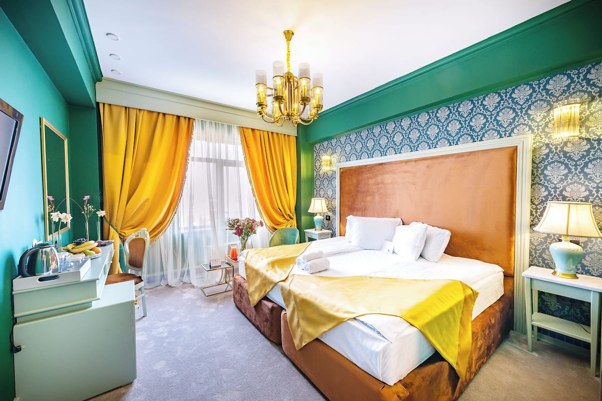 Quarto de hotel com uma cama grande, mesa de cabeceira, cômoda e um candelabro.