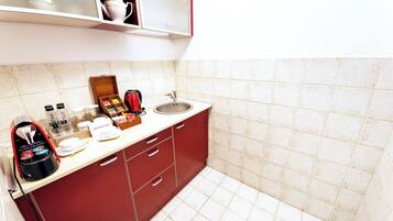 Une cuisine avec un meuble rouge, un plan de travail blanc, un évier et une machine à café.