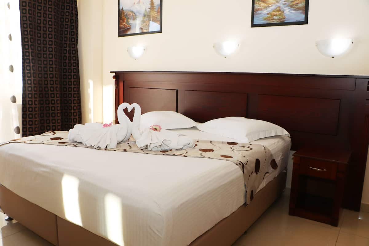 Een net opgemaakt bed met een handdoek in de vorm van een hart, een houten hoofdbord en twee wandlampen.