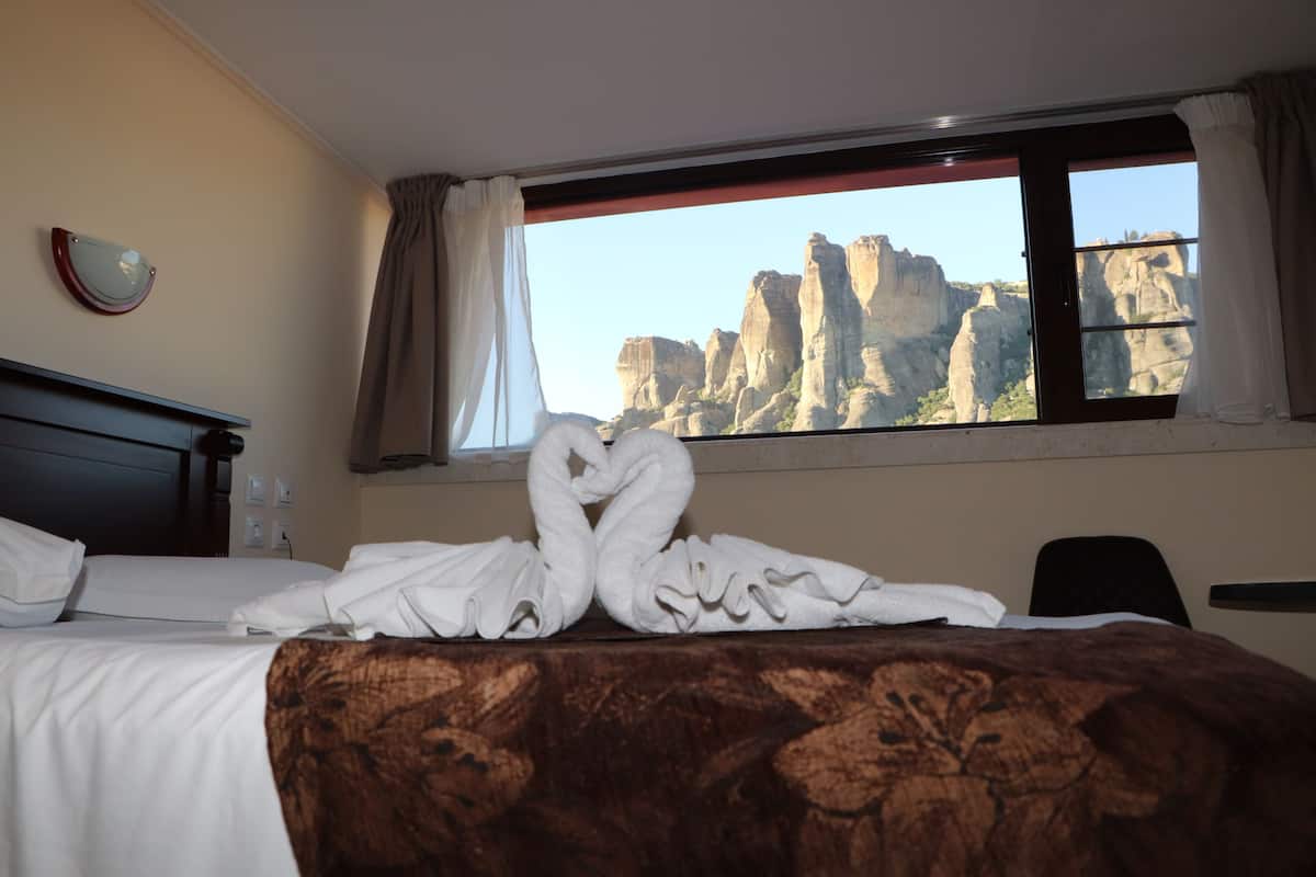 Een hotelkamer met een bed, een raam met gordijnen en uitzicht op rotsformaties.