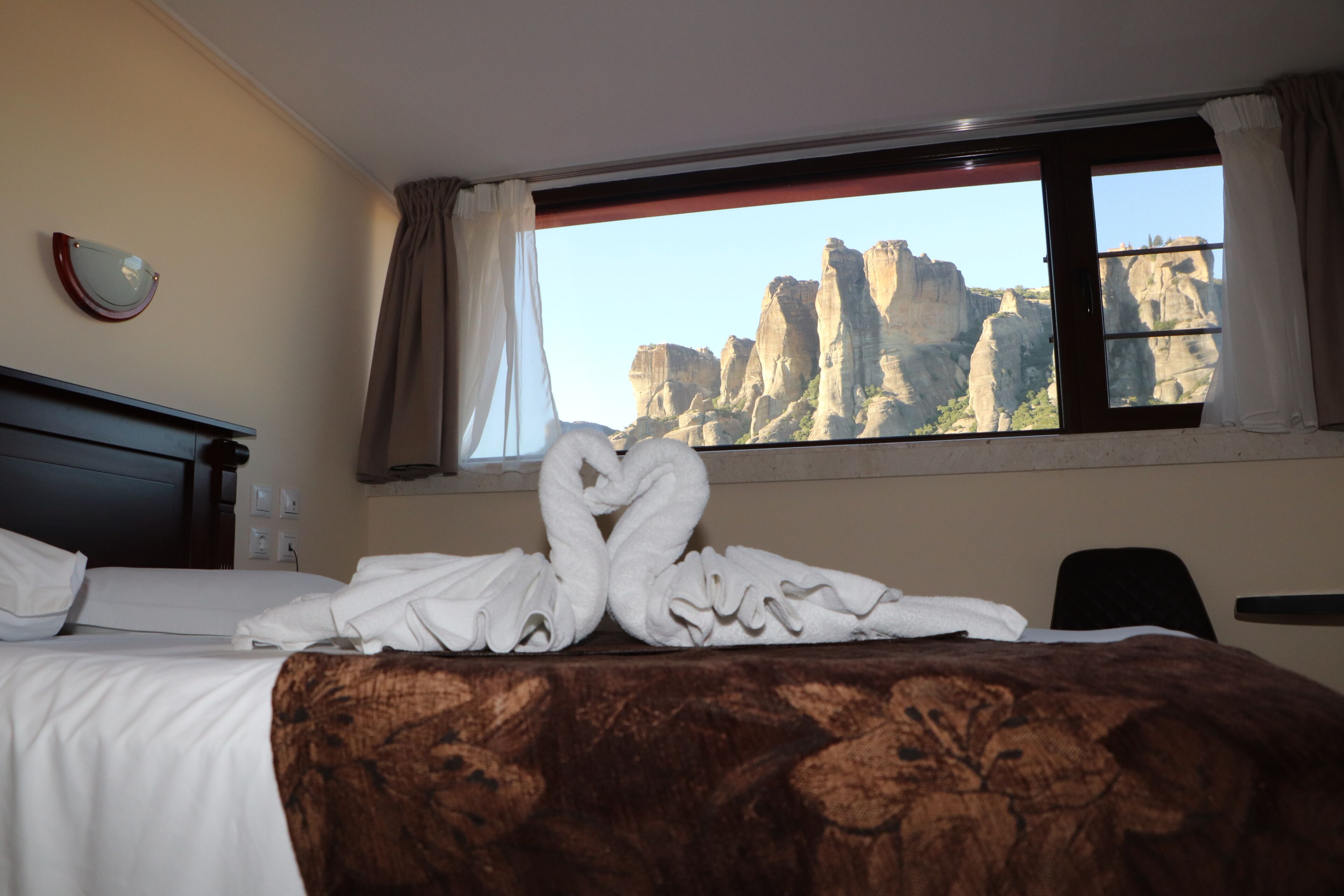 A hotel room with a bed, a window with curtains, and a view of rock formations.