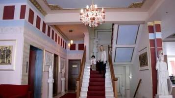 Una gran escalera con alfombra roja que conduce a una sala con candelabro y estatuas clásicas.