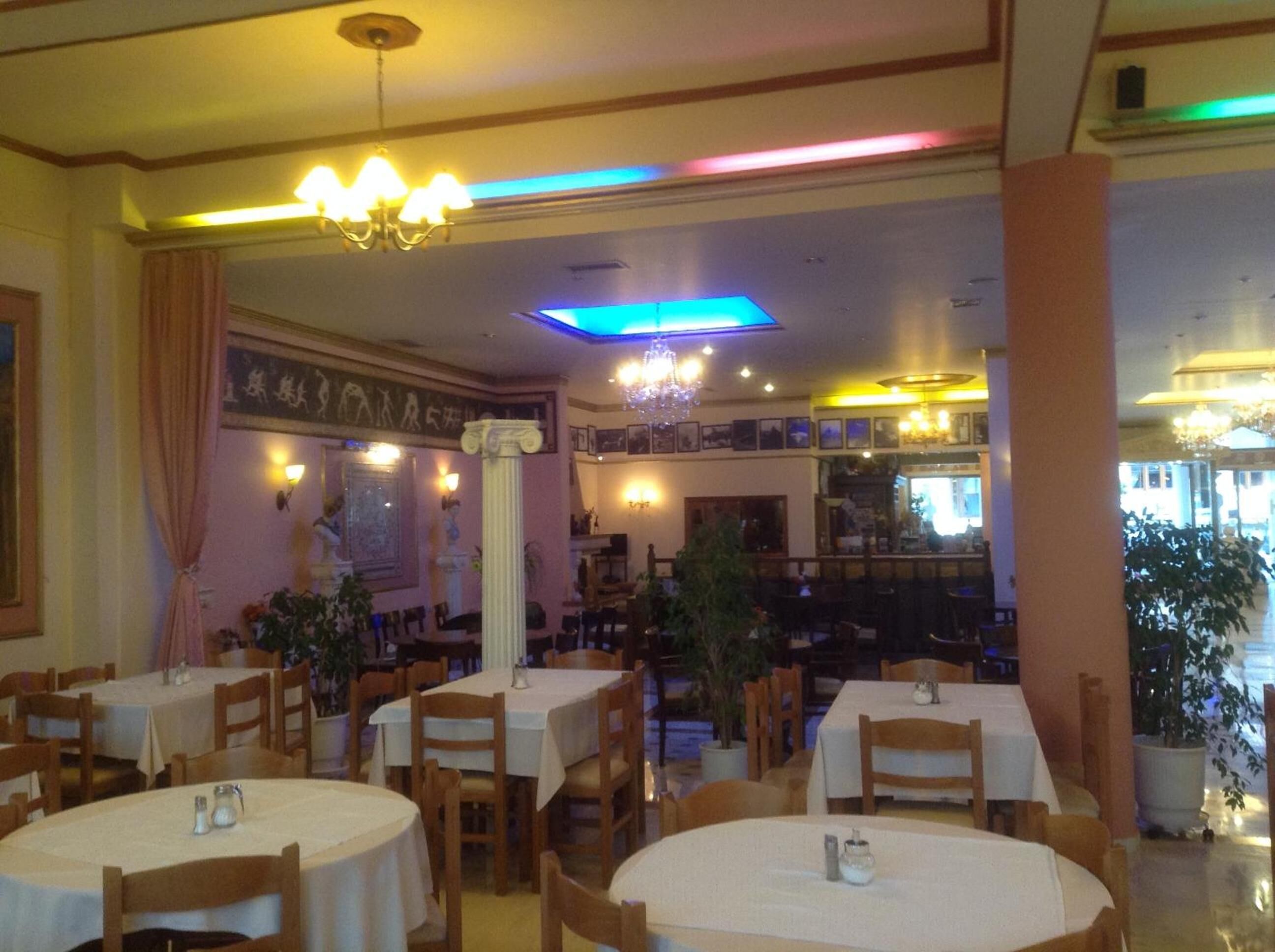 L’intérieur d’un restaurant avec des tables rondes, des chaises en bois, des lustres et des plantes en pot.