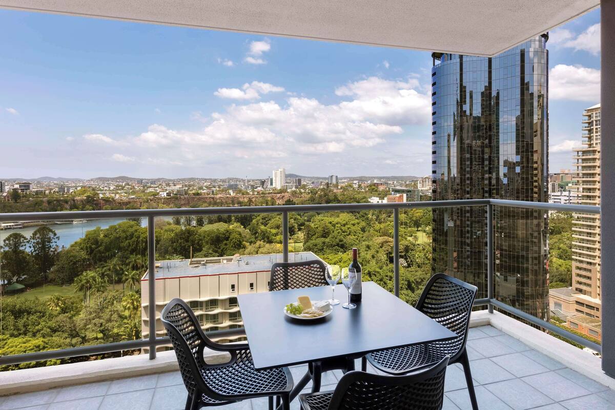 Un balcon avec une table dressée pour deux personnes, une bouteille de vin et une assiette de nourriture.
