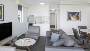 Ein modernes Wohnzimmer mit grauem Sofa, einem Flachbildfernseher und einem Essbereich mit weißem Tisch und Stühlen.