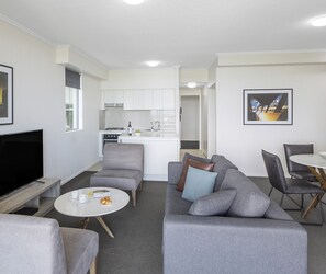 Ein modernes Wohnzimmer mit grauem Sofa, einem Flachbildfernseher und einem Essbereich mit weißem Tisch und Stühlen.