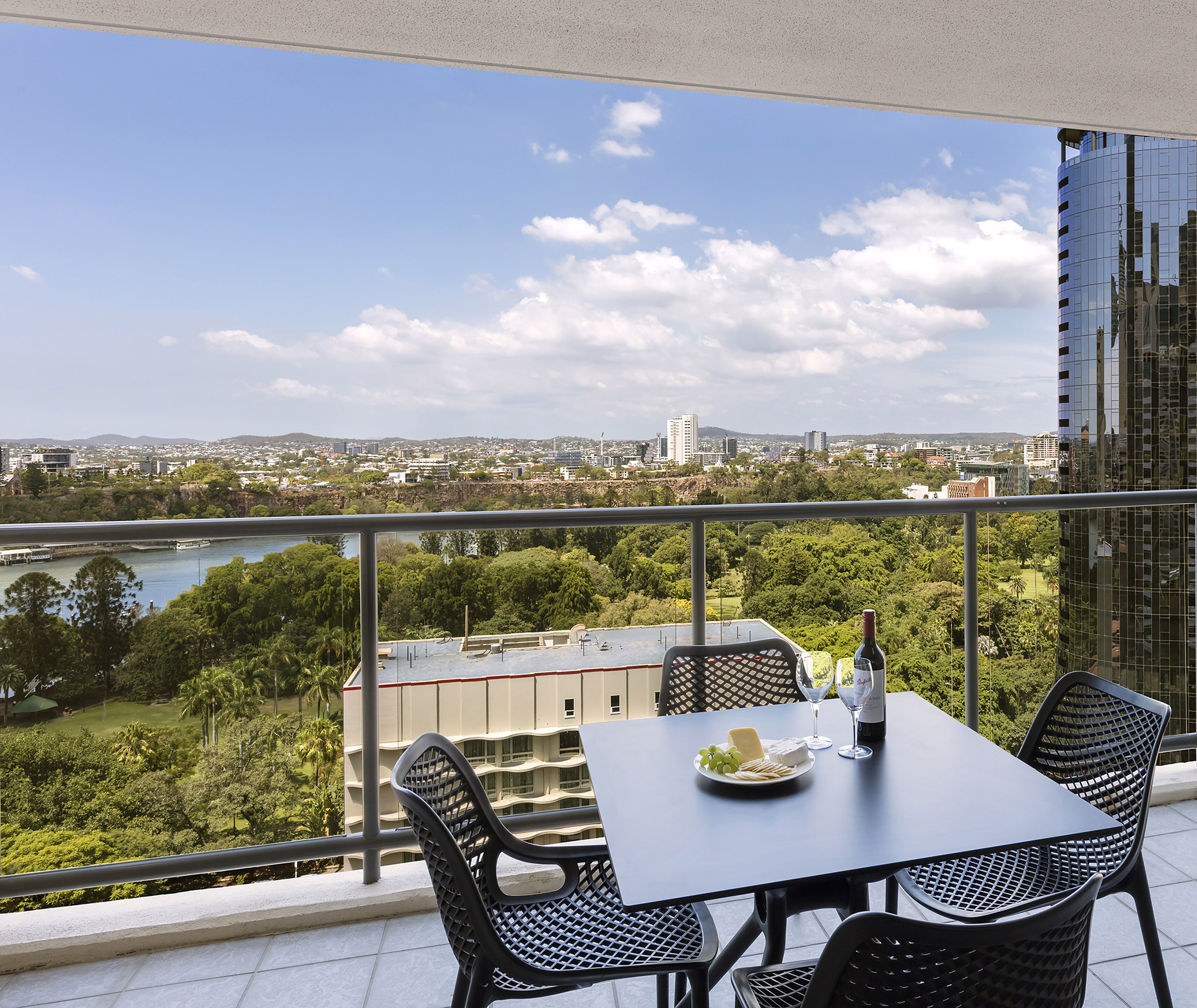Un balcon avec une table dressée pour deux personnes, offrant une vue sur le paysage urbain et une rivière.