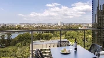 Un balcón con una mesa lista para dos personas, con vistas a un paisaje urbano y un río.
