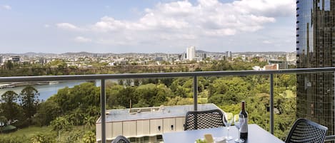 Un balcon avec une table dressée pour deux personnes, offrant une vue sur le paysage urbain et une rivière.