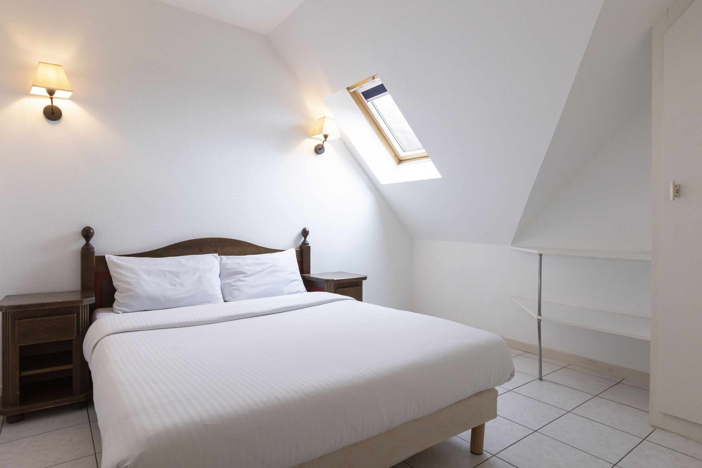 A bedroom with a large bed, two bedside tables, a nightstand, a window with a view, and a wall-mounted lamp.