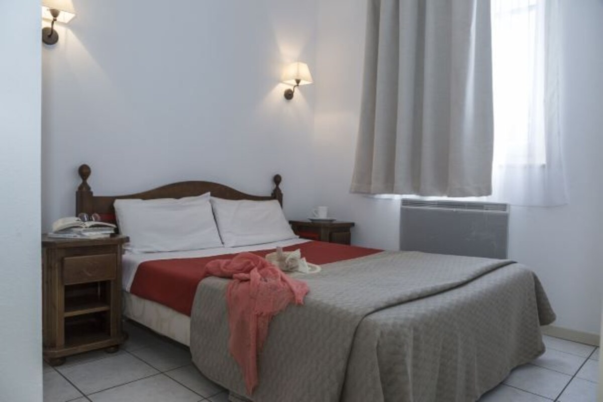 A bedroom with a wooden bed, white pillows, a red blanket, and a bedside table with a lamp.