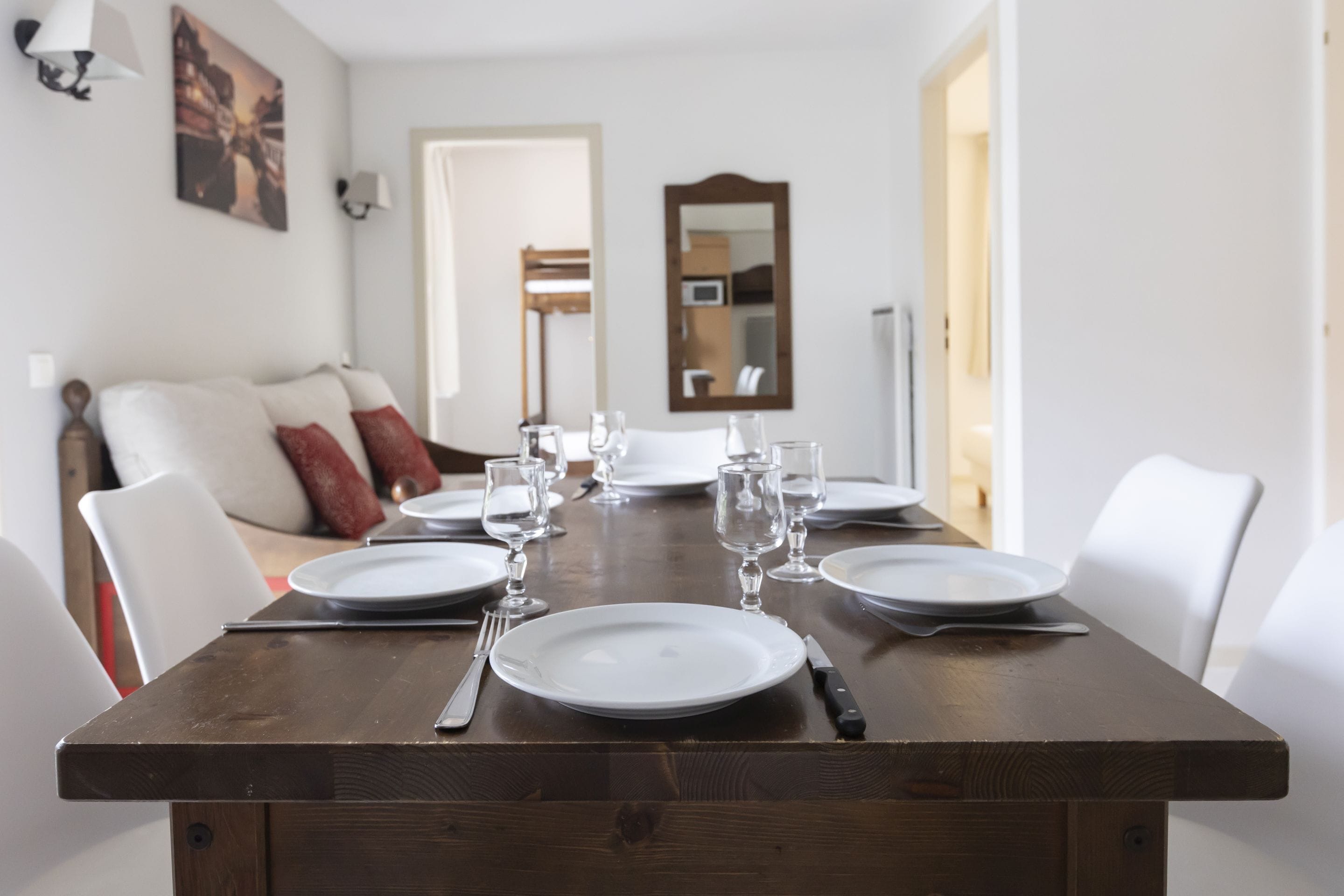 A dining table set with plates, glasses, and cutlery, flanked by white chairs.
