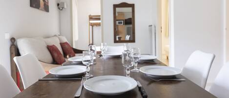 A dining table set with plates, glasses, and cutlery, flanked by white chairs.
