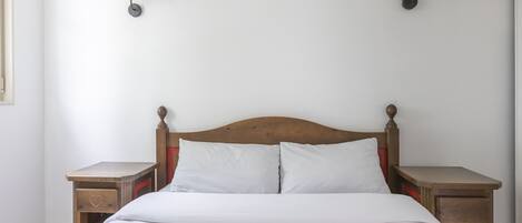 Ein ordentlich bezogenes Bett mit weißen Leinen, zwei Nachttische mit Lampen und ein Holz-Kopfteil.