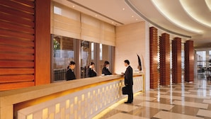 Una zona de recepción de hotel con un diseño moderno, que incluye un mostrador de recepción, varios empleados y un vestíbulo amplio con un estampado de cuadros en el suelo.