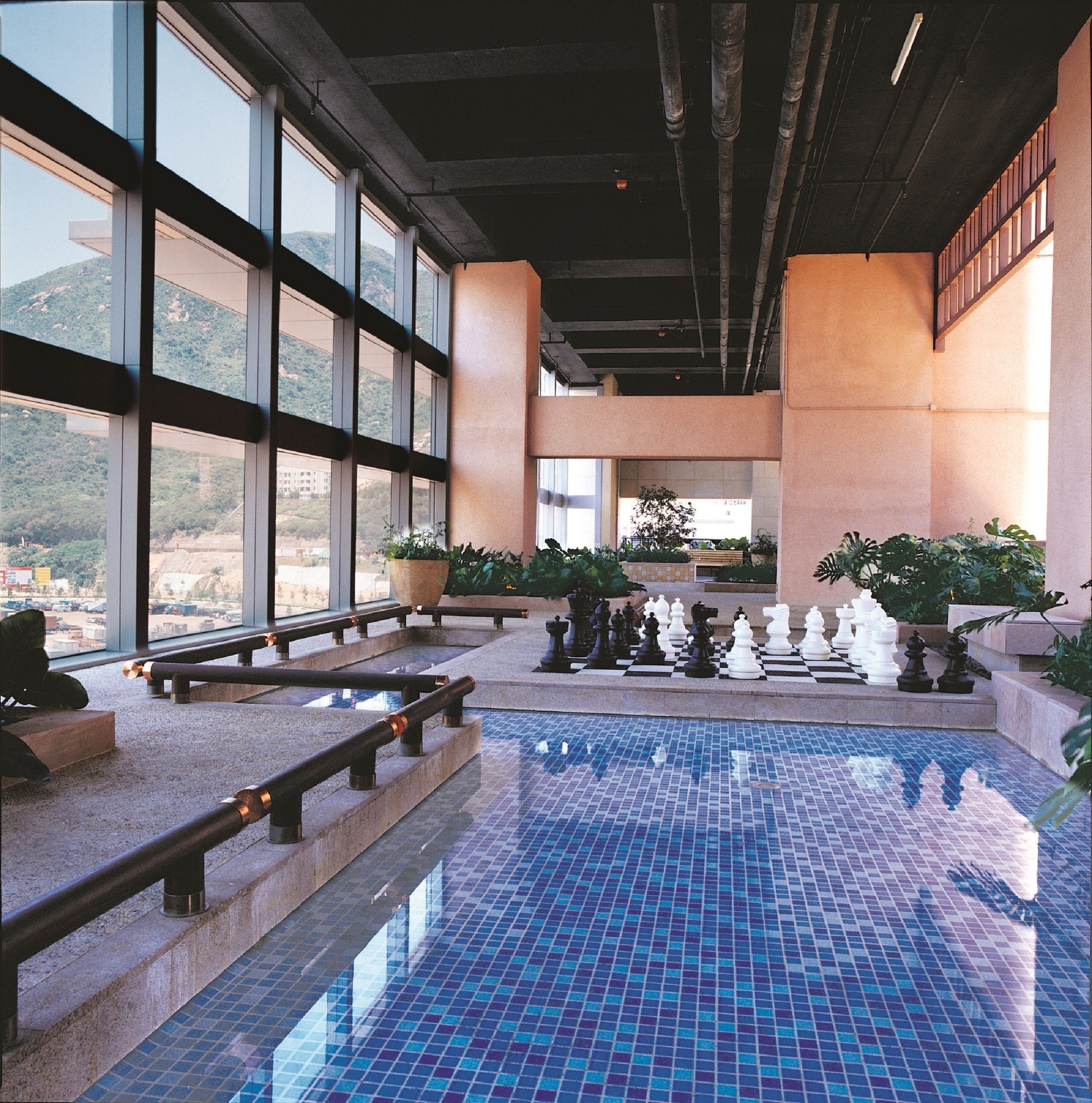 Una piscina interior con suelo a cuadros, ventanas amplias y plantas en macetas.