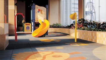 A children's play area with a slide and climbing structure, located in a corridor with large windows and a tiled floor.