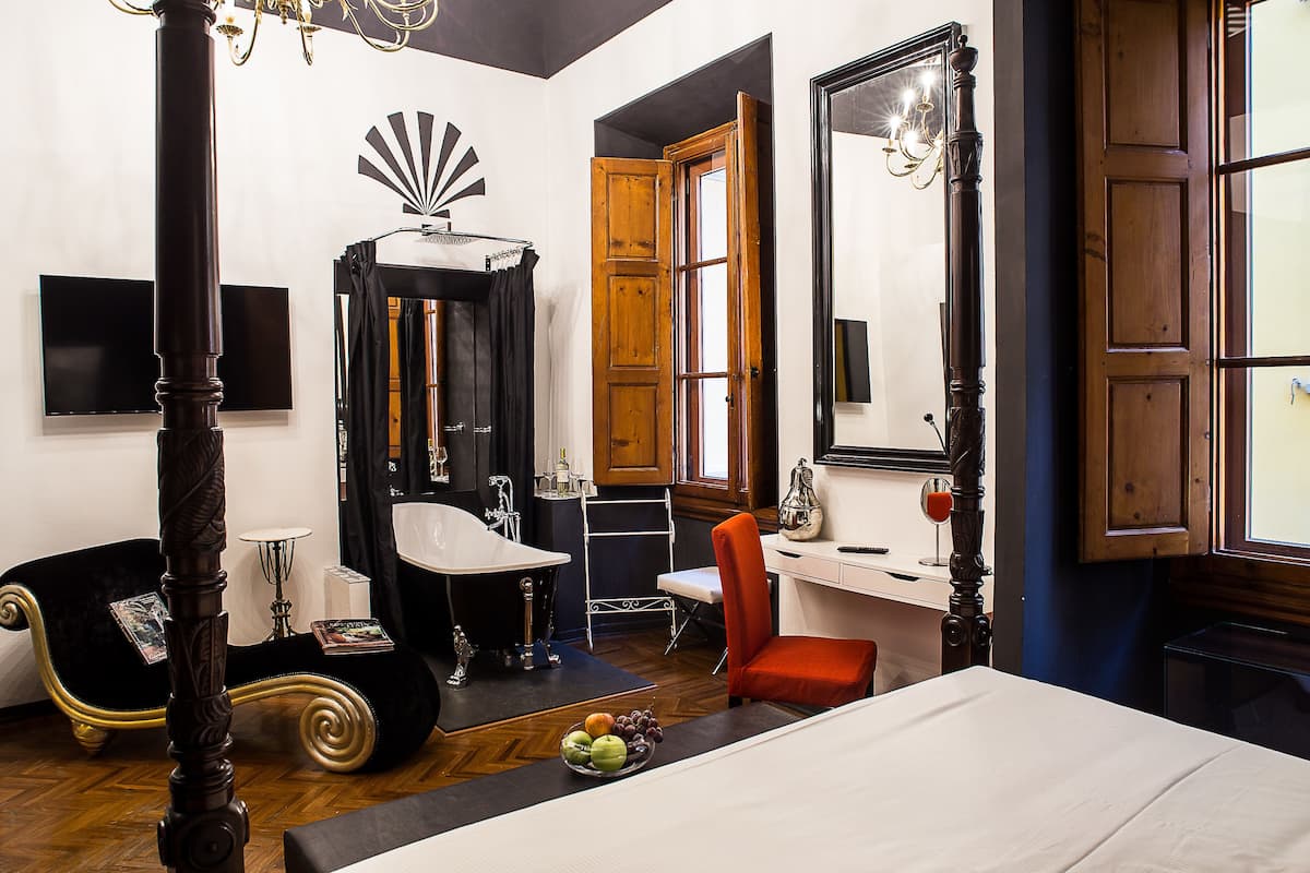 A bedroom with a four-poster bed, a vanity with a mirror, a red chair, and a wooden door.