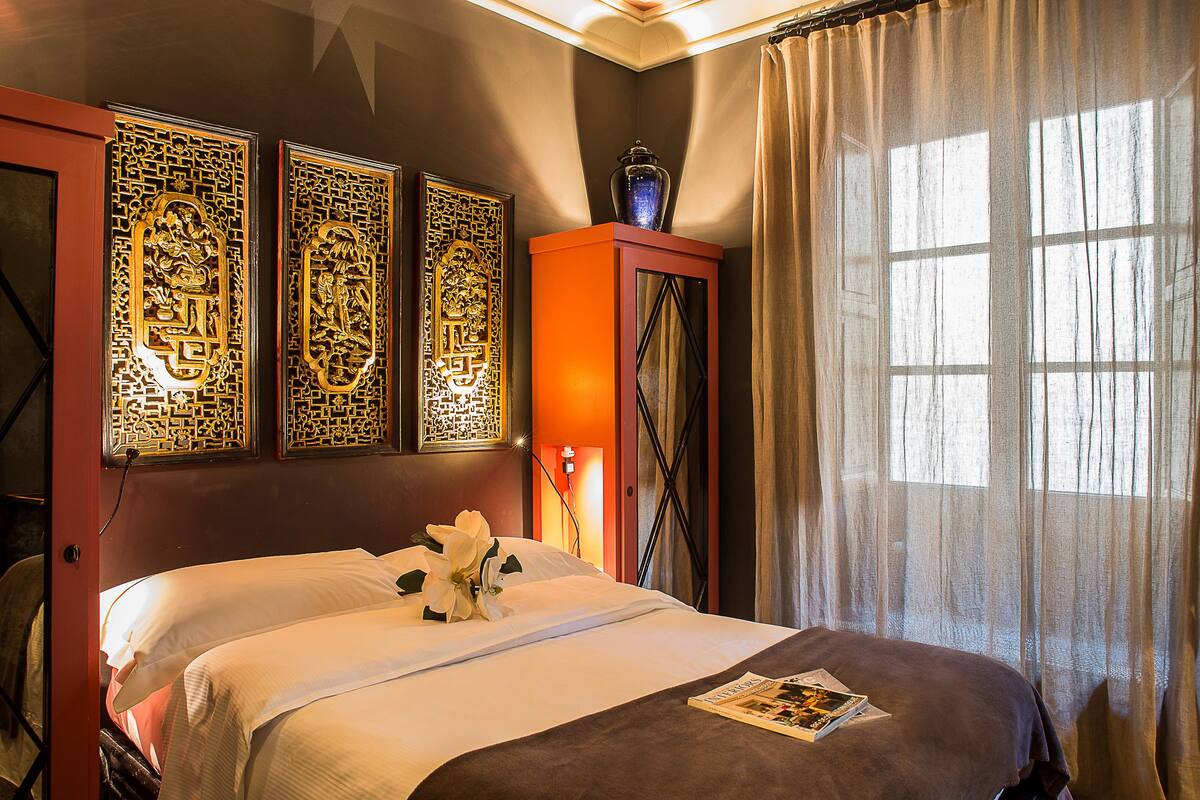 A hotel room with a bed, decorative panels, a vase, and a window with curtains.