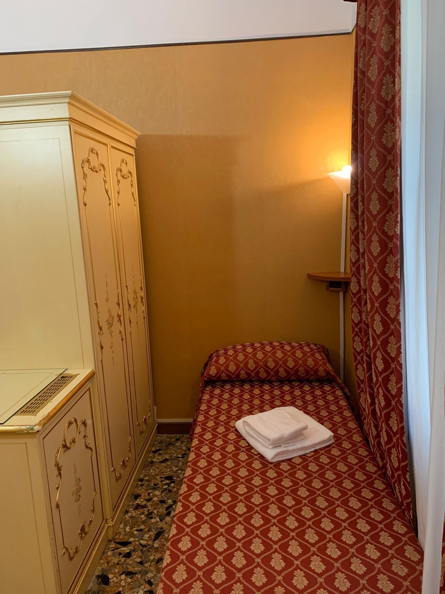 A small room with a bed, a wardrobe, and a nightstand.