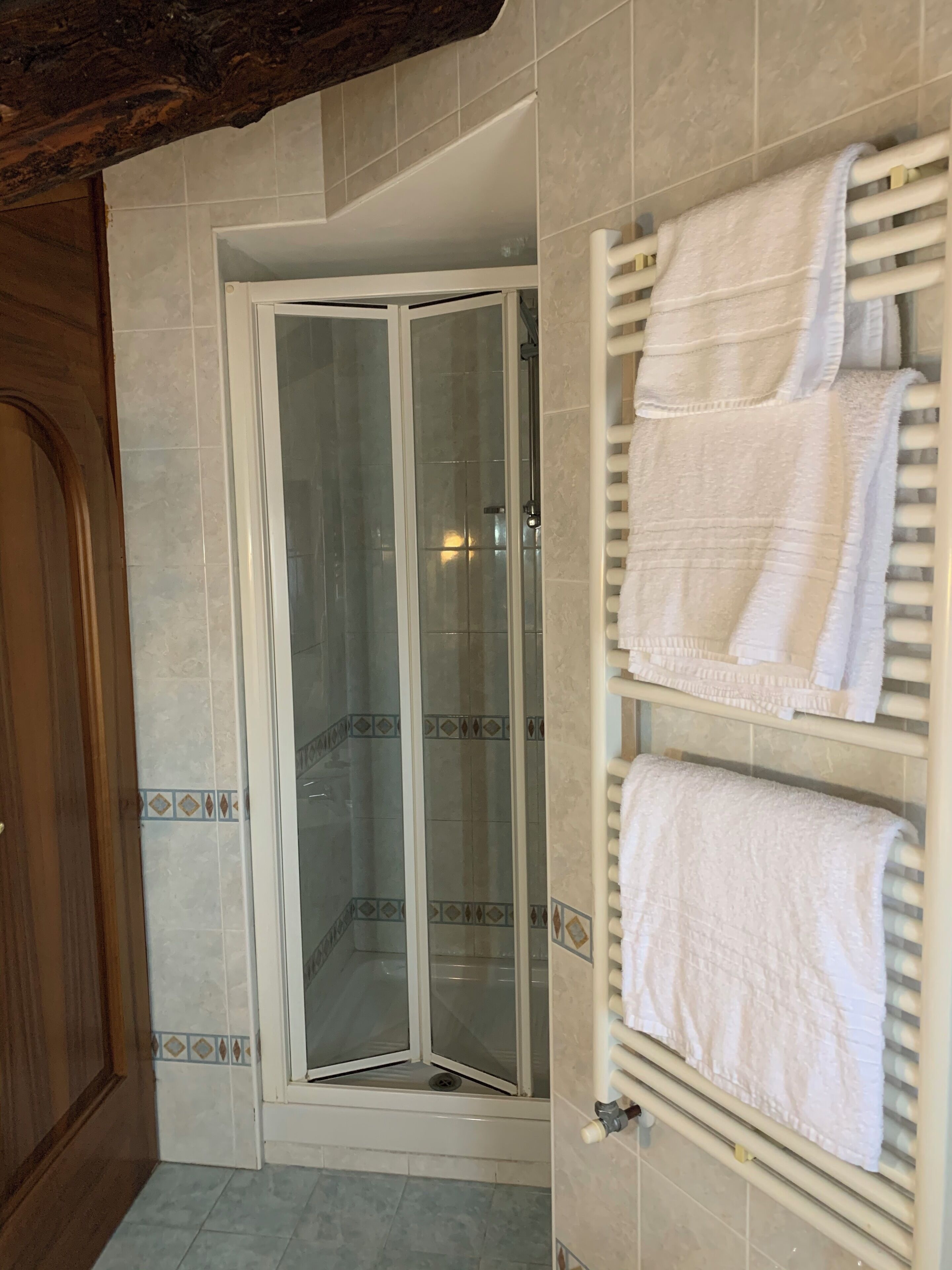 Un baño con cabina de ducha de vidrio, un perchero con toallas dobladas y azulejos estampados en las paredes.