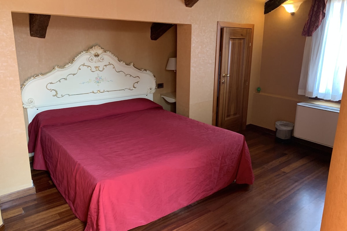 Une chambre à coucher avec un grand lit, un plancher en bois, une porte en bois et une fenêtre avec des rideaux.
