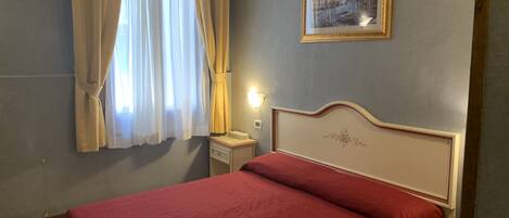 A hotel room with a bed, a nightstand, a lamp, and a painting on the wall.