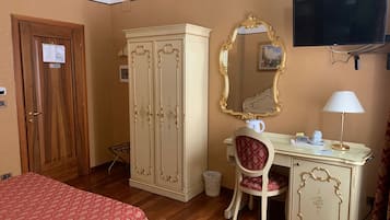 Une chambre d’hôtel avec une armoire en bois, un bureau avec une chaise, une télévision et un lit recouvert d’une couvre-lit à motifs.