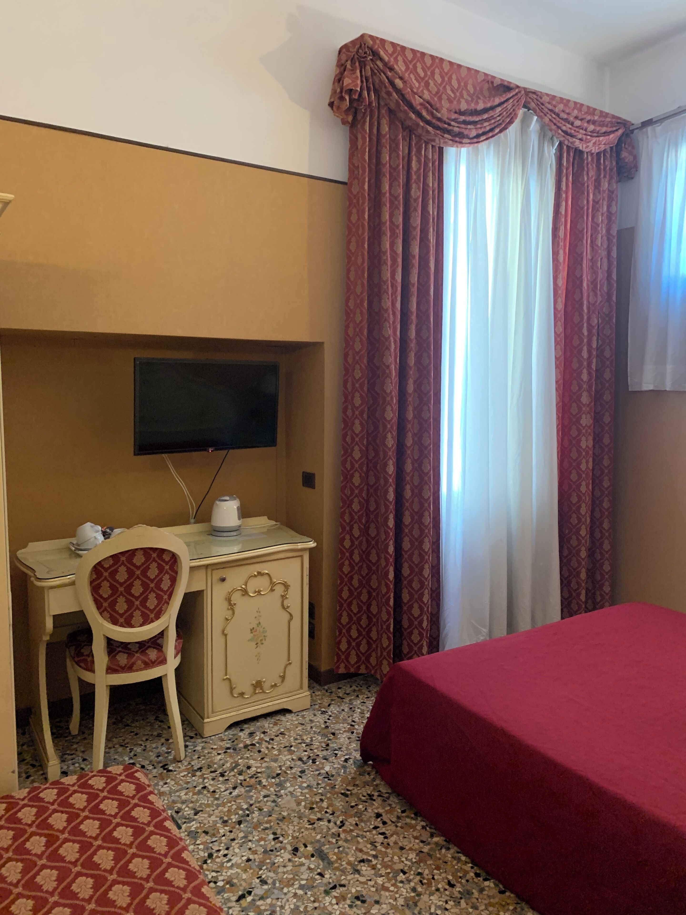 A hotel room with a bed, a desk with a chair, a television, and a window with curtains.