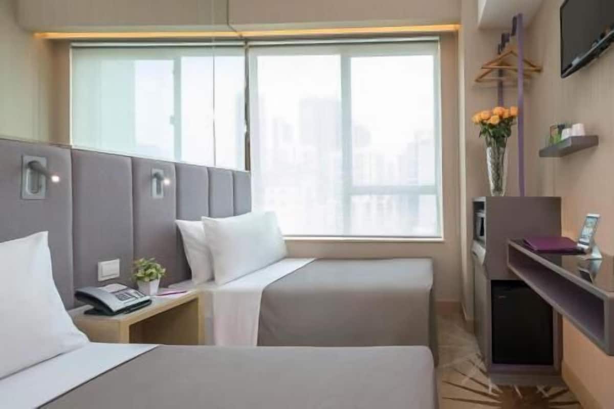 Une chambre d’hôtel avec deux lits, un bureau avec un téléphone, une petite plante, une fenêtre donnant sur un beau paysage et un téléviseur fixé au mur.