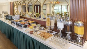 Un bufé con diversos alimentos y bebidas, un espejo con marco decorativo, y una zona de estar al fondo.