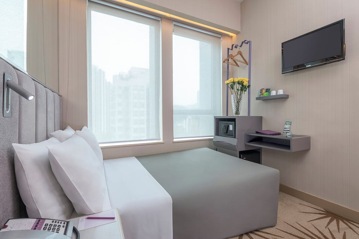Une chambre d’hôtel avec un lit, un bureau équipé d’un ordinateur, une télévision et une fenêtre donnant sur la ville.