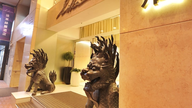 Entrada de hotel con un letrero en idioma extranjero, una recepción y dos estatuas de leones.