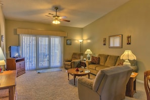 A living room with a ceiling fan, a sofa, a coffee table, a TV on a stand, and a lamp.