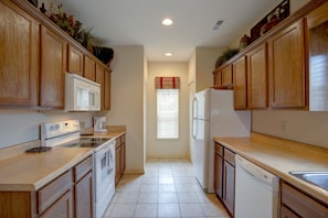 A kitchen with wooden cabinets, a microwave, stove, oven, dishwasher, and a window with blinds.