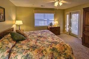 A bedroom with a floral bedspread, two bedside lamps, a wooden dresser, and a window with blinds.