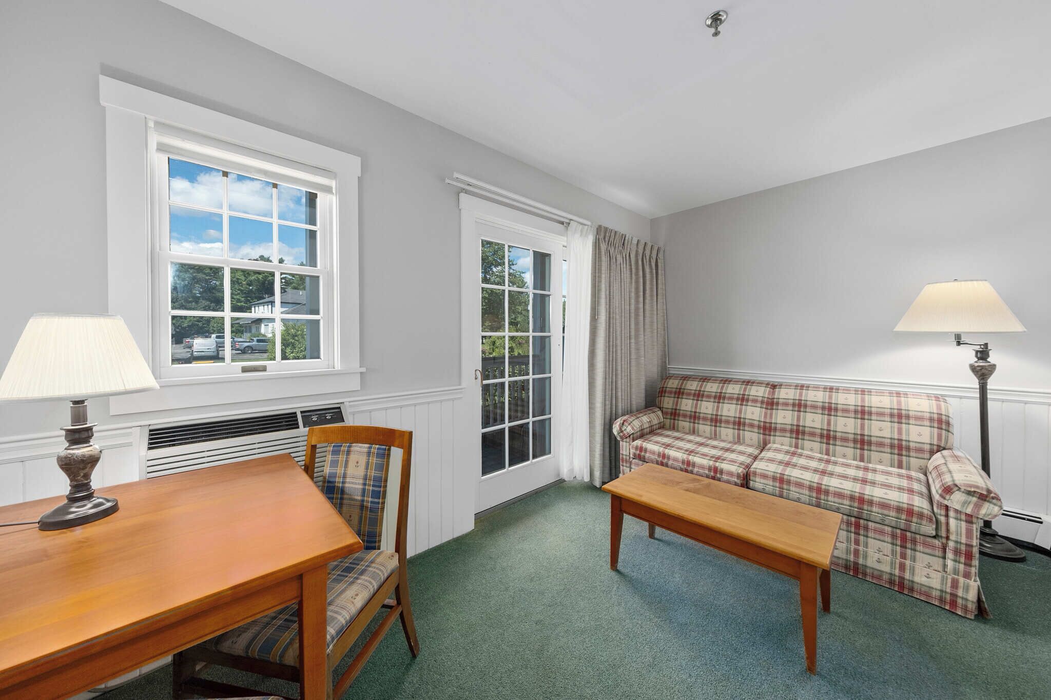 A room with a plaid sofa, a wooden table, a chair, and two lamps.