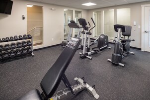 Un gimnasio con equipo de ejercicio, incluyendo cintas de correr, una banca y mancuernas.